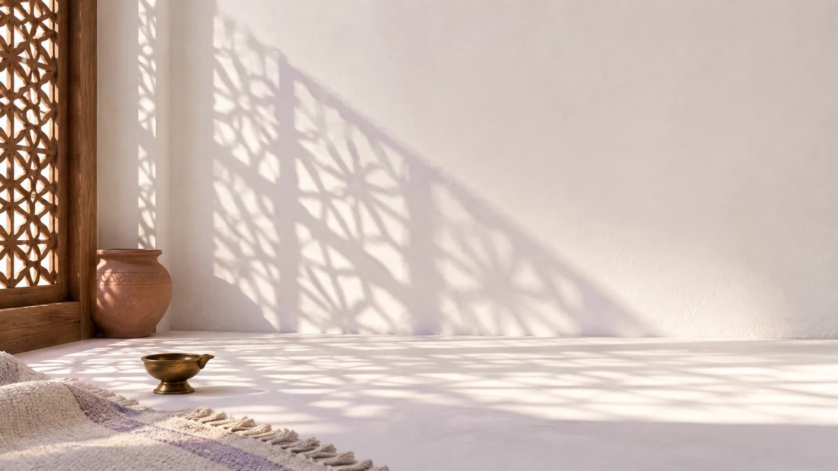Sunlight falling through a carved jaali screen, casting lattice shadows across a white wall